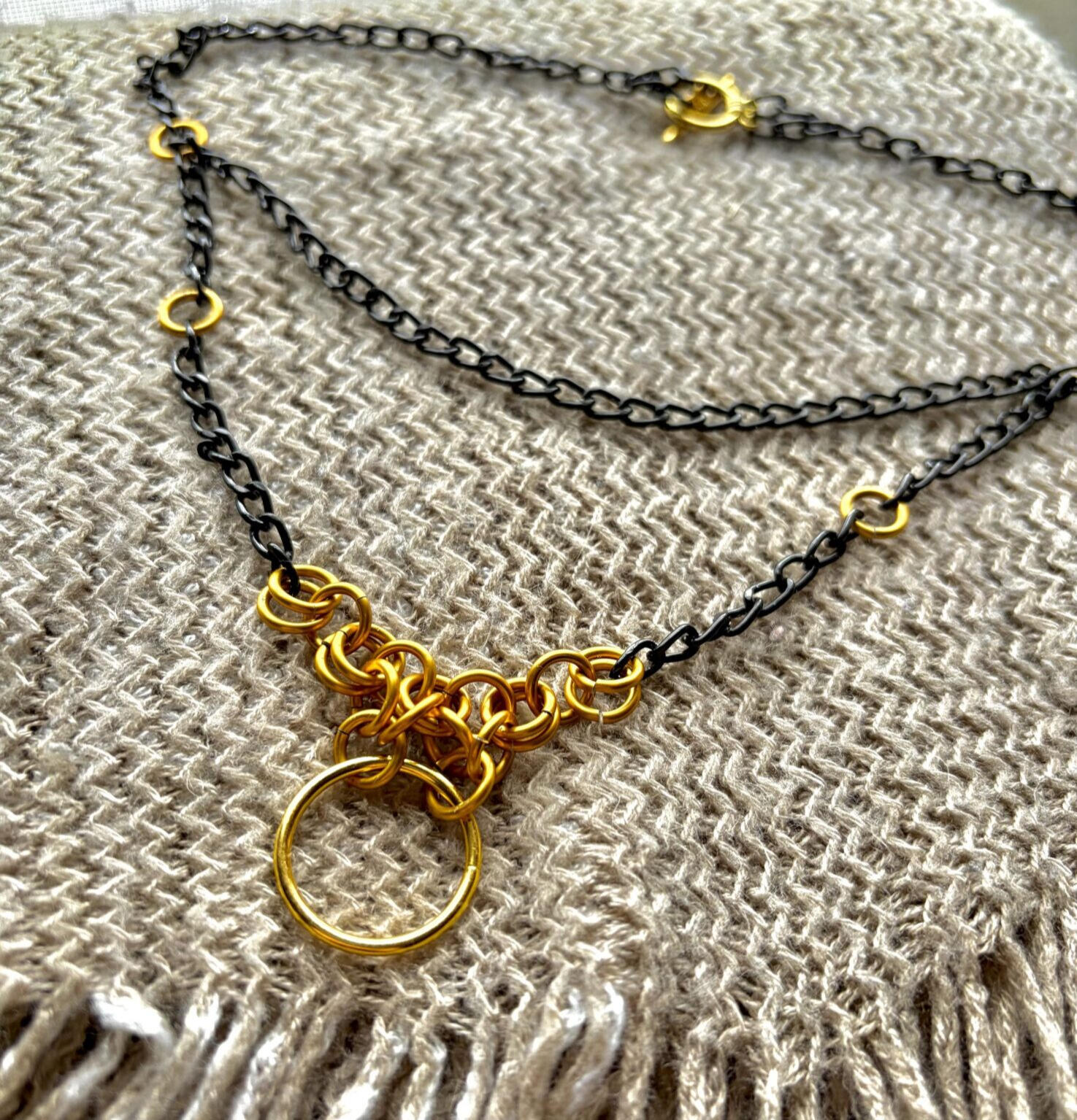 Image of a necklace with black chain and gold jumpring accents.